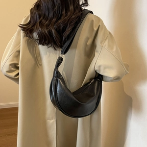 Detail of a black crescent shoulder bag with soft gloss finish on a beige trench coat
