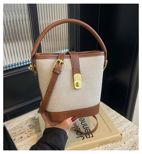 Detail of canvas bucket bag showing leather trim, gold buckle, and top handle texture