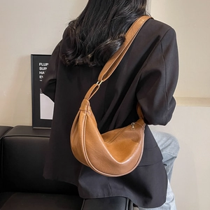 Brown leather crescent bag with smooth texture worn by a model in a professional blazer