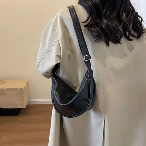 Detail of a black crescent leather bag with silver metal buckles on a slim strap