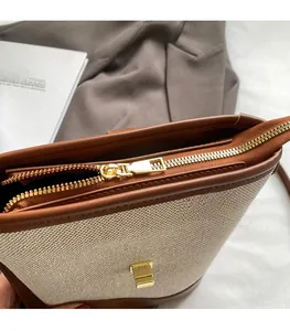 Detail of canvas bucket bag showing gold metal zipper and smooth brown leather trim