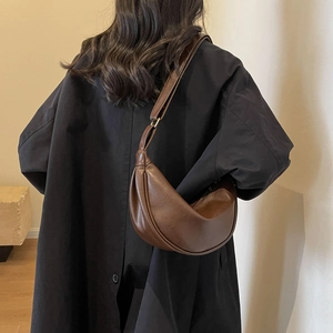 Brown hobo shoulder bag with adjustable strap worn by model in minimalist setting