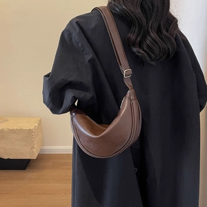 Detail of a dark brown crescent shoulder bag with adjustable strap worn by a model
