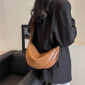 Detailed view of the brown moon-shaped hobo bag with a wide strap on a model wearing black