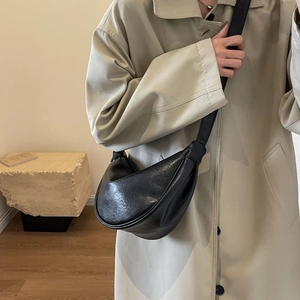 Detail of a black half-moon leather crossbody bag styled with a khaki trench coat