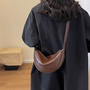 Detailed view of a brown leather crescent shoulder bag worn on a person's back