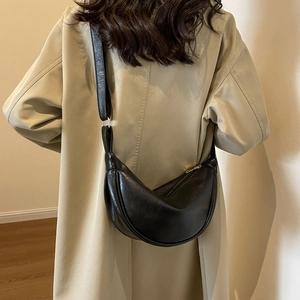 Close-up of black leather half-moon crossbody bag with wide strap on a beige coat