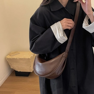 Detail view of large dark brown leather crescent bag on model in minimalist setting