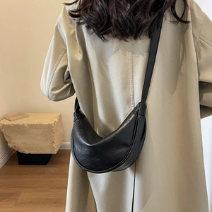 Detail view of the black leather crescent bag worn over a beige trench coat