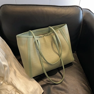 Grand cabas tissé vert avec fines bandoulières sur un fond de cuir noir élégant