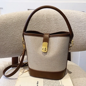 Chic canvas and brown leather bucket bag with gold clasp and adjustable strap on a chair