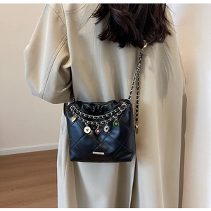 Detail of black quilted shoulder bag with golden chains and colorful enamel charms
