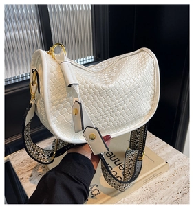 Detail of white woven texture shoulder bag featuring gold hardware and a wide graphic strap