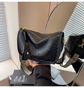 Close-up of black woven texture hobo bag with geometric patterned wide strap and gold hardware