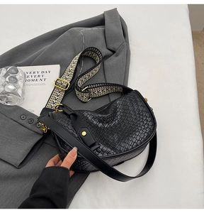 Close-up of black woven crescent bag with wide geometric patterned shoulder strap