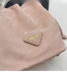 Détail du sac en tissu plissé rose avec un logo triangulaire et une inscription dorée