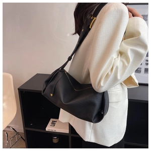 Model side view of black pebble leather shoulder bag with wide strap and gold hardware