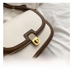 Close-up of the light gold textured metal lock on a cream and brown leather bag