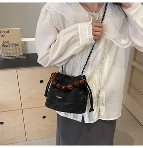 Détail du sac seau noir à cordon avec poignée en perles d'ambre et chaîne