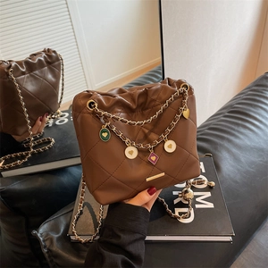 Brown quilted leather bucket bag with gold chain strap and colorful charms shown in a mirror