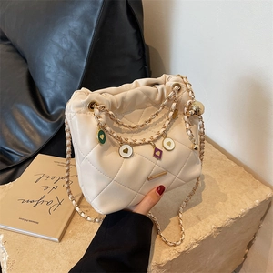 Beige quilted bucket bag with colorful heart charms and gold chain strap on stone surface