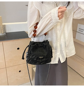 Détail du sac seau plissé noir avec poignée en perles d'ambre et logo en métal triangle