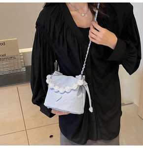 Détail du sac seau plissé bleu clair avec poignée en perles et plaque logo en métal