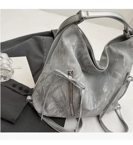 Silver pleated tote bag with bow zipper detail and adjustable strap on white surface