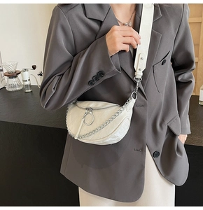 Close-up of beige half-moon crossbody bag with silver chain and wide adjustable strap