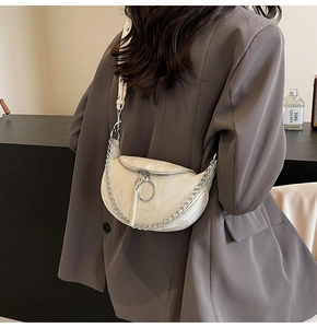 Detail of beige quilted crescent saddle bag with silver chain strap on model shoulder