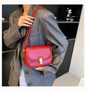 Detail of red leather crossbody saddle bag with gold metal twist lock on grey blazer