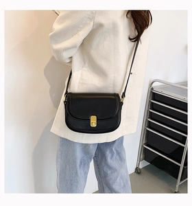 Detail of black leather crossbody saddle bag with gold metal twist lock and adjustable strap