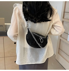 Detail of black crescent crossbody bag featuring glossy crinkled leather and silver chain