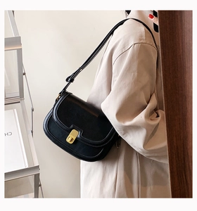 Detail shot of black leather saddle bag with gold metal clasp on a beige trench coat