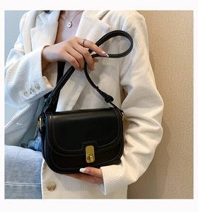 Detail of a black matte leather saddle bag with vintage gold buckle on a model