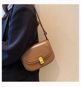 Close-up of brown matte leather underarm bag with gold metal buckle on a black blazer