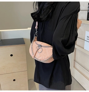 Detail of a light pink crescent crossbody bag with silver chain and metal ring zipper