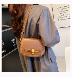 Adjustable brown matte leather saddle bag worn by a model in a modern interior setting