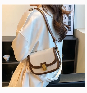Detailed view of cream saddle bag with brown trim and golden CD buckle on a model
