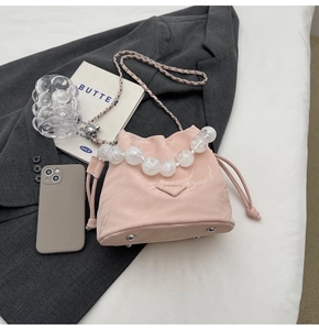 Détail du sac seau plissé rose avec poignée en perles et chaîne métal sur blazer gris