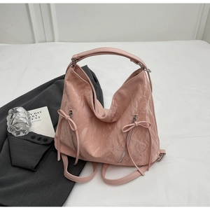 Pink crinkle texture tote bag with bow details and functional zippers on white surface