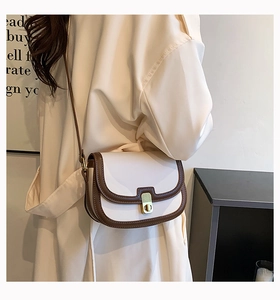 Close-up of a cream saddle bag with brown leather trim and golden clasp on a model