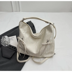 Detail of white pleated leather tote featuring decorative zippers and ribbon bow accents