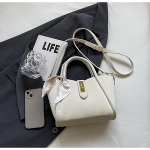 Detail of off-white lychee grain leather bucket bag with gold lock and silk scarf decoration