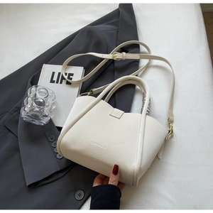 Close-up of a cream-colored bucket bag with gold hardware on a gray blazer setting