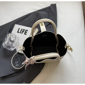 Top view of cream bucket bag with lychee leather texture and pink silk bow accessory