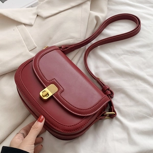 Chic burgundy saddle bag with retro gold clasp on white linens and a beige blazer