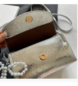Detail of silver metallic crossbody bag featuring magnetic buckles and pearl ornament