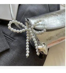 Macro detail of a silver handbag featuring a pearl bow and heart-shaped metal pendant