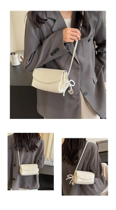 Close-up of beige crossbody bag with pearl bow and heart pendant on faux leather